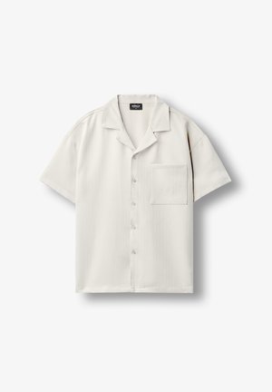 Camisa de manga corta color beige claro con botones, un bolsillo en el pecho y cuello relajado, extendida sobre un fondo blanco.