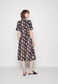 Vestido preto floral com mangas curtas, cintura ajustada com laço e saia até o joelho adornada com padrões em rosa e verde.