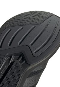 Semelle de chaussure de sport noire, présentant des motifs en caoutchouc texturé, des rainures pour l'adhérence et une section centrale renforcée pour la durabilité.