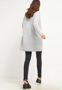 Cardigan lungo grigio a strisce con spacchi laterali, abbinato a jeans skinny neri e sandali neri con tacco spesso. Tessuto dal tocco morbido.