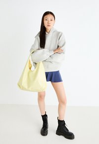 Šedá oversized mikina, modrá sukně, žlutá kabelka typu hobo. Černé šněrovací combat boots s tlustou podrážkou. Hladké materiály, minimalistický design.