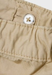 Tejido beige con una textura arrugada, que presenta un botón de plástico transparente con un diseño de cuatro agujeros y costura a lo largo del borde.
