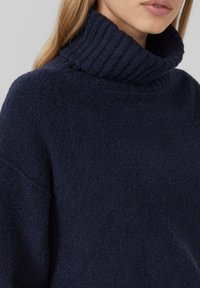 Navy-blauer Rollkragenpullover aus weichem, strukturiertem Stoff mit einem gerippten Kragen und legerem Schnitt, der eine entspannte Silhouette präsentiert.