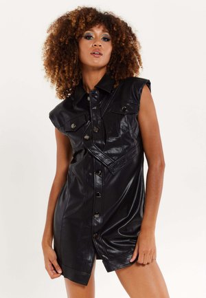 Black faux leather dress with a collar, short sleeves, front buttons, and two chest pockets. Features a unique diagonal seam and side slit.