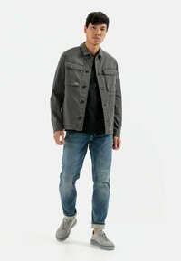 Grå jakke med to brystlommer, knaplukning, båret over en sort top, parret med lyseblå jeans og grå sneakers. Simpelt design.