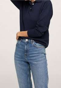 Pullover blu navy con colletto e placket a due bottoni, abbinato a jeans chiari a vita alta con tasche frontali e lavaggio chiaro.