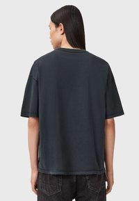 Ciemnoszary, oversize T-shirt z krótkimi rękawami, okrągłym dekoltem, surowymi krawędziami i widocznymi detalami szwów. Materiał wydaje się miękki i teksturowany.