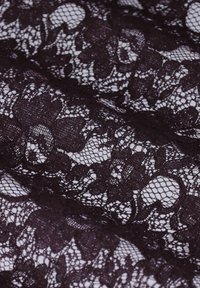 Black floral lace fabric with intricate open weave, showing detailed flower and leaf patterns against a light background.
