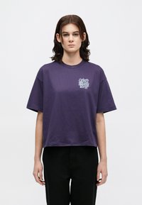 Fioletowy krótki T-shirt wykonany z bawełny, z krótkimi rękawami i okrągłym dekoltem. Zawiera biały nadruk graficzny na lewej części klatki piersiowej.