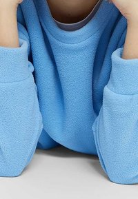 Maglione in pile azzurro chiaro con un fit rilassato, ampie maniche e collo a giro. Il tessuto ha una texture morbida e una leggera lucentezza.