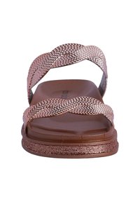 Sandalias de oro rosa con tiras metálicas texturizadas, suela plana marrón y acentos brillantes. El diseño presenta una forma cruzada en la parte superior.