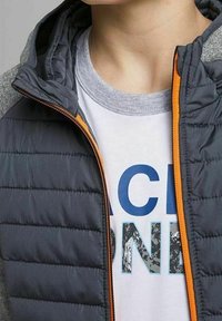 Puchowa kurtka w szaro-granatowej kolorystyce, z pomarańczowym zamkiem. Noszona na białym t-shircie z niebieskim graficznym napisem.