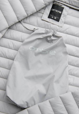 Giacca a vento grigia chiara con texture trapuntata e cappuccio regolabile. Accompagnata da una borsa di stoccaggio grigia abbinata con logo "ombre".