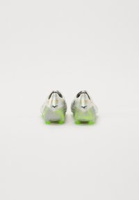 Schoenen met een metallic zilveren bovenkant, zwarte accenten en levendige groene noppen. Beschikt over een gestructureerd oppervlak voor grip en ventilatiegaten.