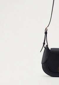 Black leather crossbody bag with a curved shape, textured surface, flap closure, and thin adjustable strap. Gold-tone hardware accents.