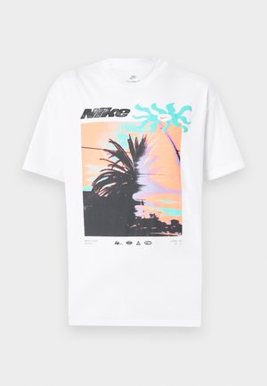 Biele tričko Nike s grafikou siluet palmových stromov na pozadí pastelového oranžovo-tyrkysového západu slnka, čierne logo Nike nad tým.