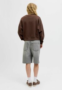 Bruine oversized sweatshirt met een ronde hals, gecombineerd met lichtgrijze denimshorts. De shorts hebben twee achterzakken en rauwe zomen.