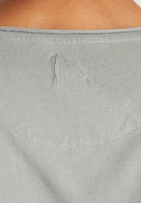 Grijze T-shirt met een gladde, zachte textuur, voorzien van subtiele gebogen naaddetails en een kleine geborduurde accent op de achterkant van de halslijn.