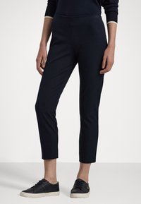 Navyblauwe, slimfit broek met een gladde textuur, enkellang en een elastische tailleband. Gecombineerd met zwarte sneakers met crèmekleurige zolen.