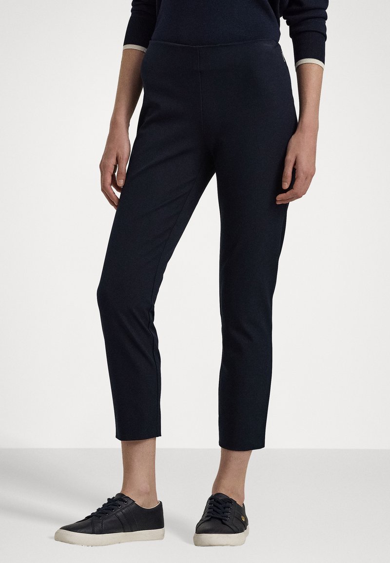 Navyblauwe, slimfit broek met een gladde textuur, enkellang en een elastische tailleband. Gecombineerd met zwarte sneakers met crèmekleurige zolen.