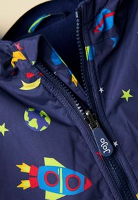 Marineblauer Jacke mit Reißverschluss, die mit bunten, weltraumthemen Mustern verziert ist: Raketen, Planeten, Sterne und Monde. Der Stoff sieht leicht und glatt aus.
