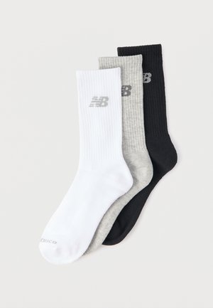 Három New Balance sportzokni fehér, szürke és fekete színekben, egy világos háttéren átfedésben elrendezve.