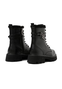 Stivali alla caviglia in pelle nera con colletto in pelliccia testurizzata, lacci frontali, zip laterale e cinturini decorativi con dettagli in fibbia. Suole in gomma spessa.