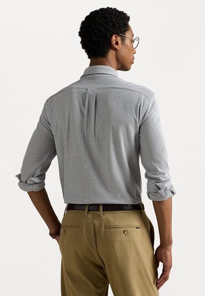 Navy and white striped button-up shirt made of cotton, with rolled sleeves. Paired with tan trousers that have two back pockets and a belt.