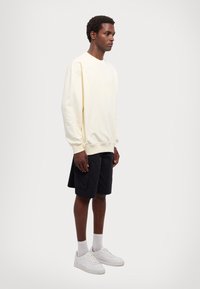 Világos sárga, oversized pulóver, bordás mandzsettákkal, fekete sortszerű alsóval és fehér sportcipővel párosítva. Pamut keverék, laza fazon, minimalista dizájn.