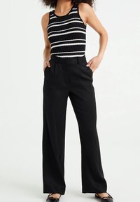 Svarta vida byxor med hög midja, tillsammans med en ribbad linne med horisontella svartvita ränder. Slät textur.