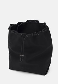 Sac seau en toile noire avec fermeture à cordon, accents en métal et logo de la marque visible à la base. Surface texturée. Design élégant.