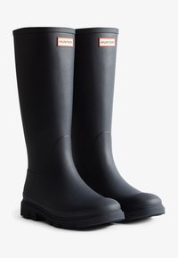 Bottes de pluie en caoutchouc noir avec des semelles texturées, de tiges hautes et des logos HUNTER sur des étiquettes rouges près du sommet. Fini lisse et design à bout arrondi.