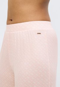 Light pink joggers made of soft fabric, featuring a subtle pattern and an elastic waistband with a small gold "BOSS" logo accent.