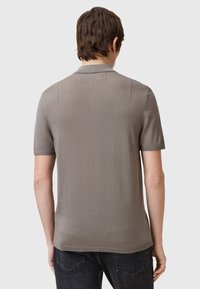 Kortärmad polo i ljusgrått tyg med en slät yta, med en klassisk krage och subtila sömdetaljer på ryggen.