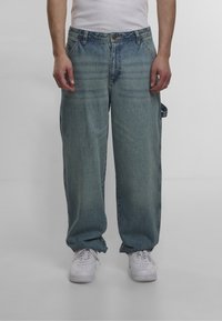 Light blue denim wide-leg jeans featuring a button and zipper closure, side pockets, and a slightly faded finish. Worn with white sneakers.