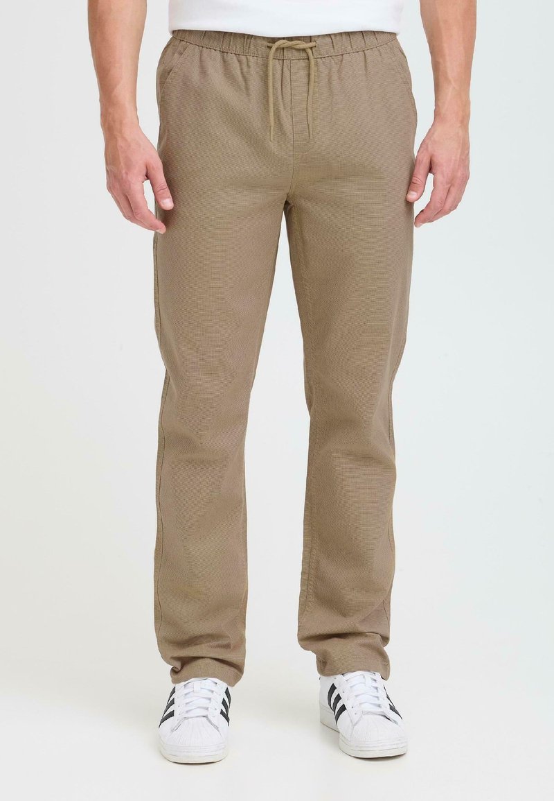 Pantalons marron, texturés, avec une taille élastique et un cordon de serrage, dotés de poches latérales, associés à des baskets blanches avec des rayures noires.