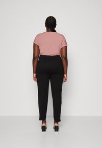 Vue arrière d'une personne portant un t-shirt à manches courtes rose clair et un pantalon noir taille haute avec une texture lisse et des poches arrière remarquables.