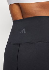 Crne tajice visokog struka od rastezljivog materijala, sa toniranim Adidas logom i ravnim šavovima za udobnost i izdržljivost.
