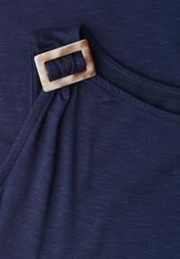Tissu bleu marine rassemblé et maintenu par une boucle rectangulaire beige effet écaille près d'une couture d'encolure.