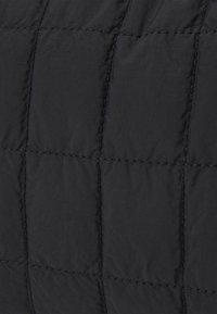 Tessuto trapuntato nero con una texture liscia presenta motivi quadrati, rinforzati da cuciture a contrasto lungo le cuciture.