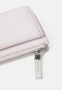Ružová kožená peňaženka s hladkou textúrou, so zipsom a striebornou visačkou so zaslúženým nápisom "Calvin Klein". Kompaktný obdĺžnikový dizajn.