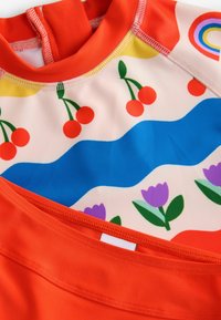 Felgekleurde zwemkleding met een rode kraag, met een gemusterd lichaam met kersen, golven en tulpen op een lichte achtergrond.