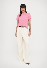 Ροζ κοντομάνικη μπλούζα φορεμένη με λευκό παντελόνι καμπάνα ψηλόμεσο. Διαθέτει μαύρη ζώνη και παπούτσια με animal print. Απλός σχεδιασμός.