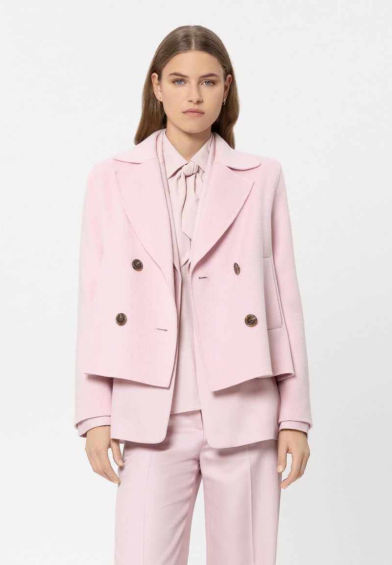 Doppelreihiger rosa Wollblazer mit Reverskragen, braunen Knöpfen und seitlichen Taschen, kombiniert mit einer passenden Bluse und Hose.