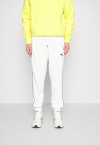 Vita joggerbyxor med dragsko i midjan, svarta sidostips och en liten svart logotyp. Matchas med en klar gul sweatshirt och vita sneakers.