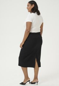 Falda midi negra con una cinturilla elástica, con una abertura en la parte trasera. Combinada con una camiseta blanca ajustada y mule de tacón negro.