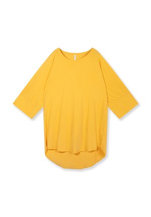 Camicia gialla a maniche lunghe, vestibilità larga, con polsini ampi e orlo arrotondato, più lunga sul retro, mostrata su sfondo bianco.