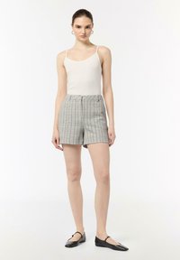 Graue karierte Shorts mit hoher Taille, kombiniert mit einem enganliegenden weißen Tanktop. Schwarze flache Schuhe runden das Outfit ab.