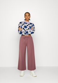 Sweater de malha colorido com padrões e design cropped. Calças largas rosas soltas com cintura elástica, combinadas com ténis brancos.