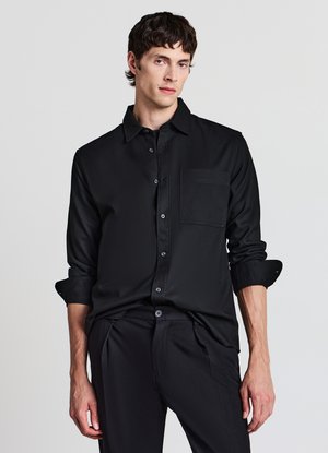 Camicia nera a maniche lunghe con bottoni, in tessuto liscio con taschino sul petto e polsini arrotolati, abbinata a pantaloni scuri coordinati.